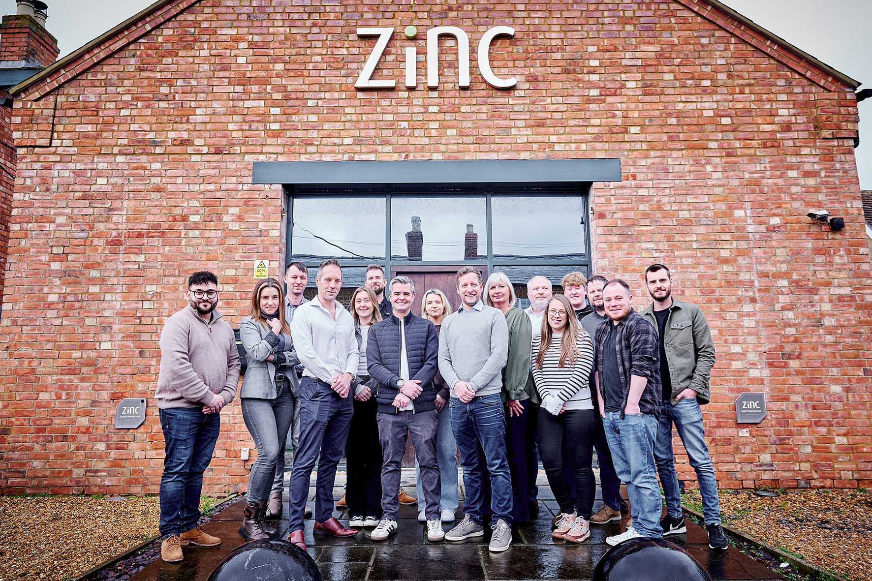 Group of coworkers posing outside a red brick building with 'zinc' signage above.