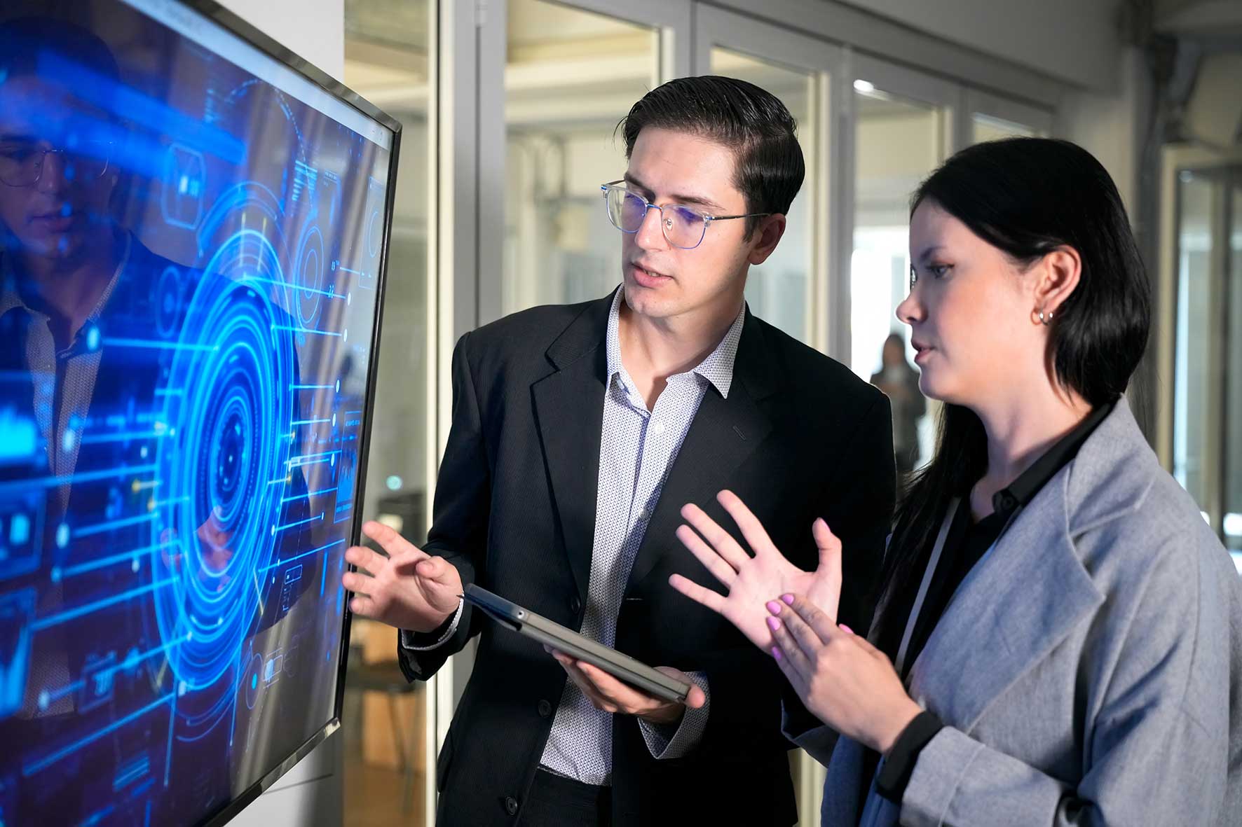 Two professionals in business attire analyze a large blue holographic screen in a modern office.
