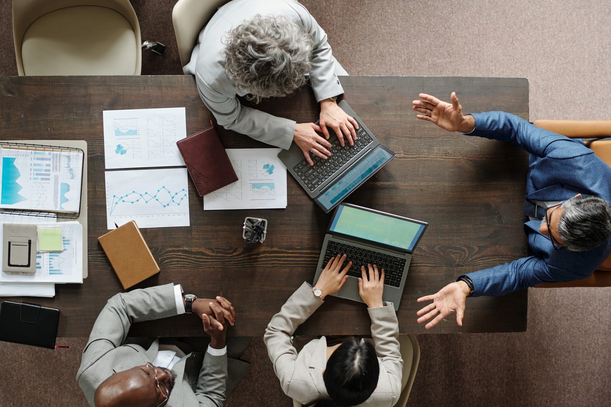 Business professionals discussing a business acquisition around a table with laptops and financial documents.