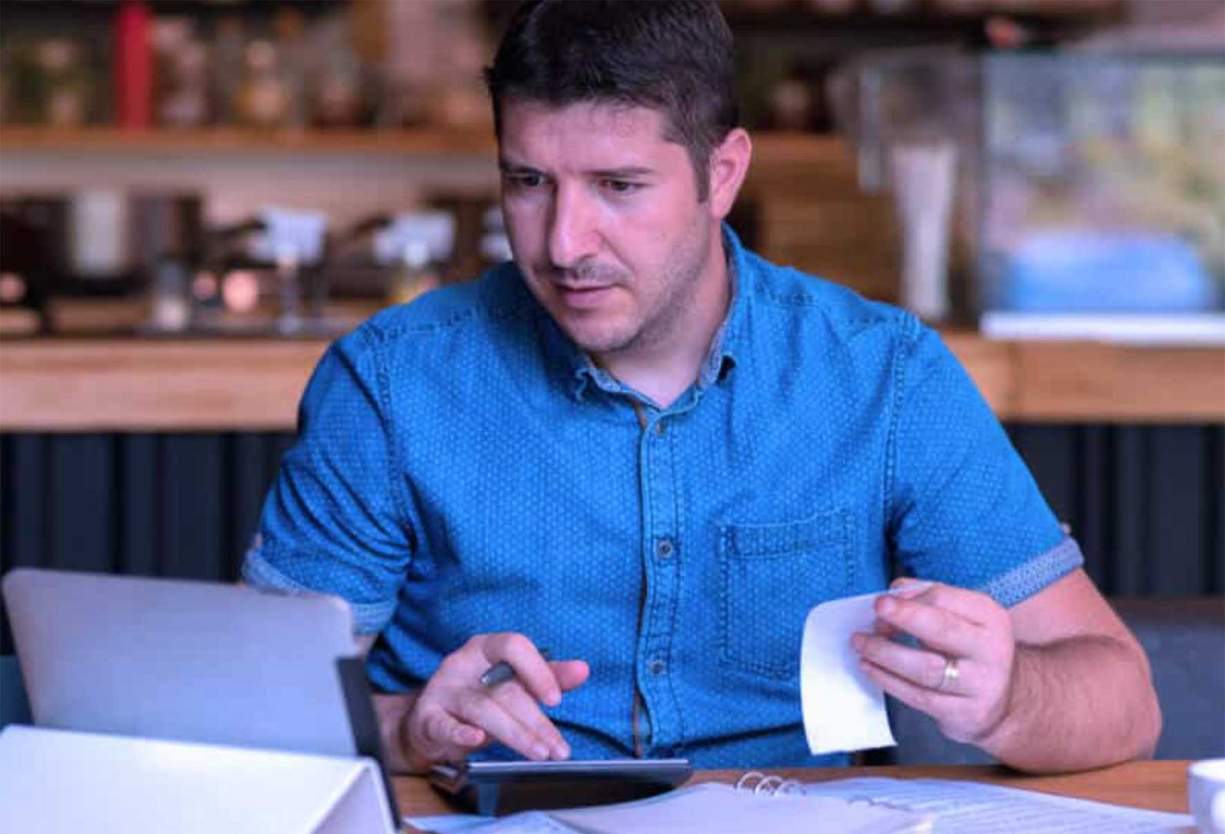 Man reviewing paperwork with a calculator and laptop at a table