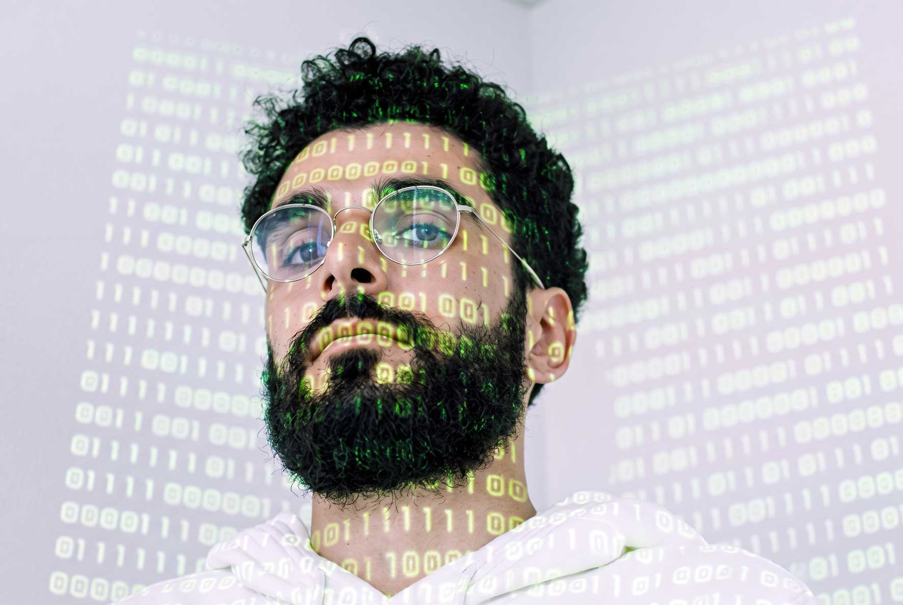 Man wearing glasses with binary computer code projected across his face, illustrating AI and digital skills training.